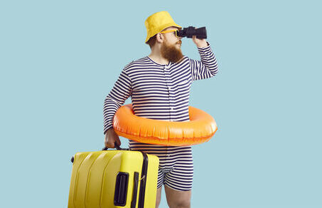 Funny Man With Suitcase And Inflatable Circle Looks Through Binoculars On Light Blue Background.